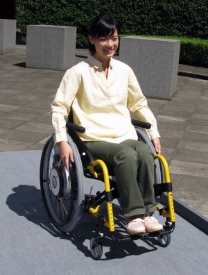 「JWX-2」を装着した車いす。車輪中央のハブにフラットなACモーターを内蔵している。設計上は傾斜6度の坂を登坂できるそうだが、腕力があればどんな坂でもOKだとか。ただし下りは注意 「JWX-2」を装着した車いす。車輪中央のハブにフラットなACモーターを内蔵している。設計上は傾斜6度の坂を登坂できるそうだが、腕力があればどんな坂でもOKだとか。ただし下りは注意