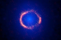 アルマ望遠鏡（オレンジ）とハッブル宇宙望遠鏡（青）で観測したSDP.81。アルマ望遠鏡では重力レンズ効果により引き伸ばされたSDP.81の姿が、完全な円形に見えている。ハッブル宇宙望遠鏡では重力レンズの原因となっている手前の銀河が見えている。また、アルマ望遠鏡の解像度がハッブル宇宙望遠鏡を上回っていることもわかる。Credit: ALMA (ESO/NAOJ/NRAO); B. Saxton NRAO/AUI/NSF; NASA/ESA Hubble Space Telescope 