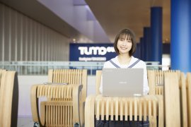 TUMO Gunmaに設置された机と椅子が一体となったオリジナル家具「TUMOBILE」に座るアンバサダーの藤崎ゆみあさん　※藤崎ゆみあさんの「崎」は立つ崎(たつさき)が正式表記。以下も同様